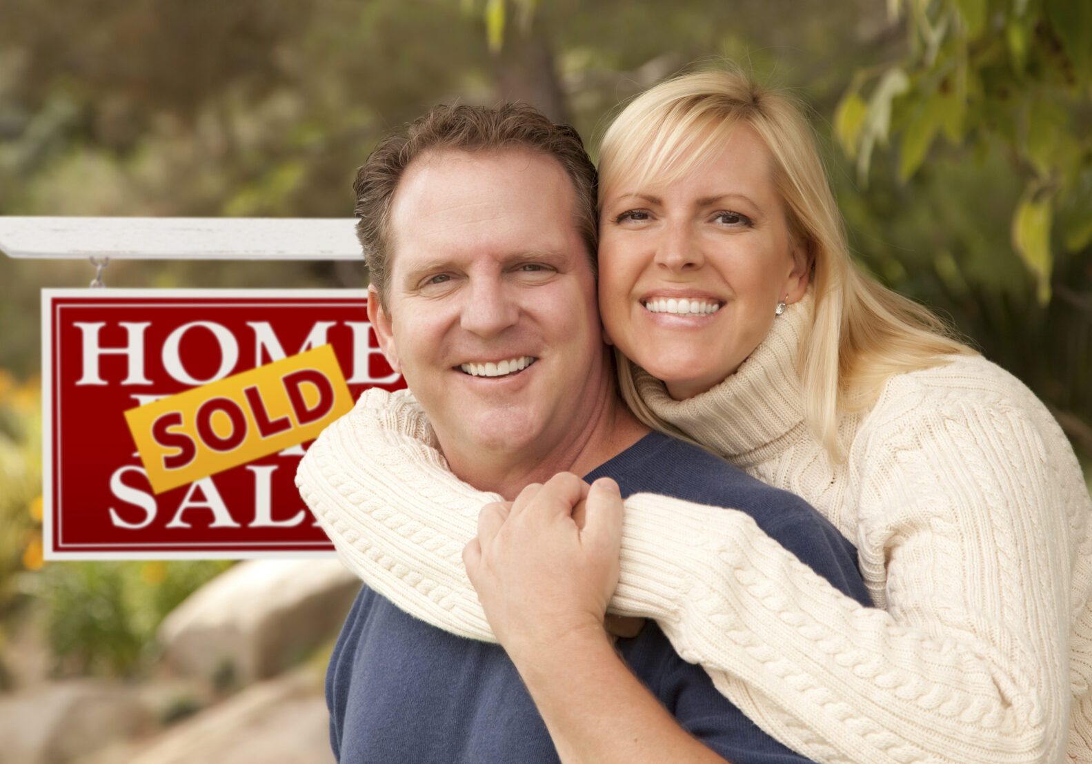 Happy Attractive Caucasian Couple in Front of Sold Real Estate Sign.